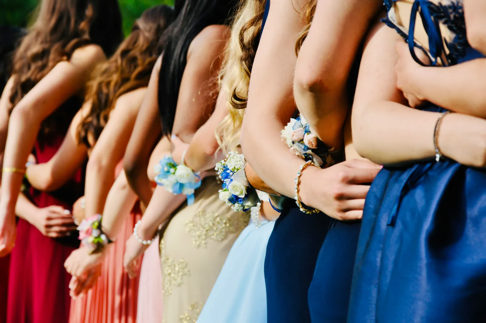 Teenagers in prom dresses and suits gathered beside a party bus before a dance